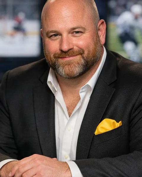 Marty "Five Yards" Kowalczyk, AI-generated news desk anchor: shaved head, ginger beard, black blazer with a yellow pocket square